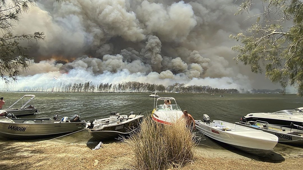Boats are pulled ashore as smoke and wildfires rage behind Lake Conjola, Australia on Thursday [Robert Oerlemans via AP]