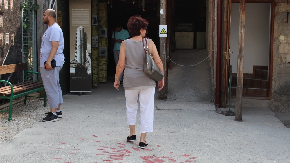 Tyra’s grandma walking over a Sarajevo Rose – mortar scars filled with red resin – in the courtyard outside the Tunnel of Hope [Photo courtesy of Tyra Bosnic]