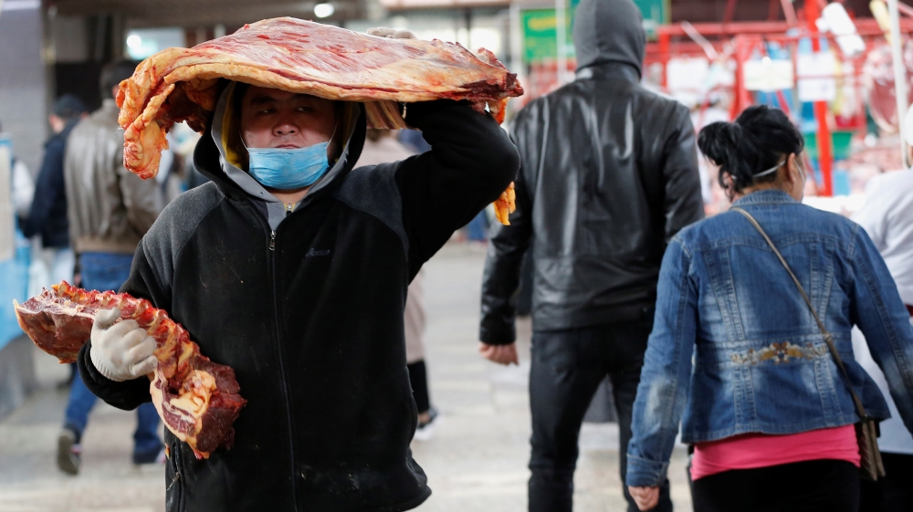 A worker wearing a protective face mask carries meat at a local food market in Almaty