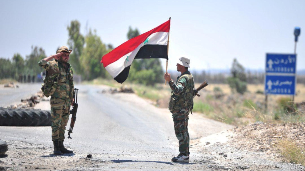 A member of forces loyal to Syria''s President Bashar al-Assad holds the national flag as another one gestures in al-Ghariya al-Gharbiya in Deraa province, Syria in this handout released on June 30, 20