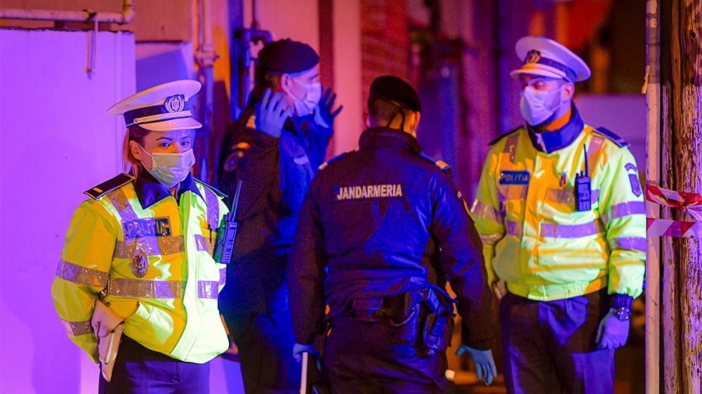 Illuminated by police car lights, a female police officer, left,  wearing a protective mask stands at a roadblock in the vicinity of one of the hospital where COVID-19 infected patients are under trea