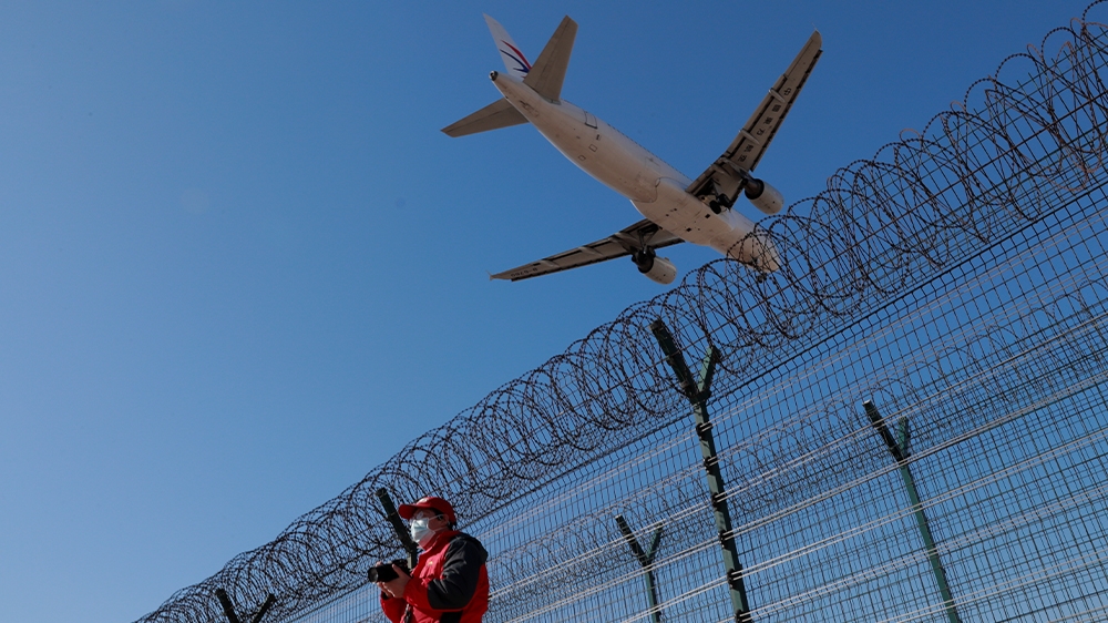 A man wearing a protective mask stands at a fence surrounding Beijing Capital International Airport. The country is now seeing more imported cases than ones that have originated locally.