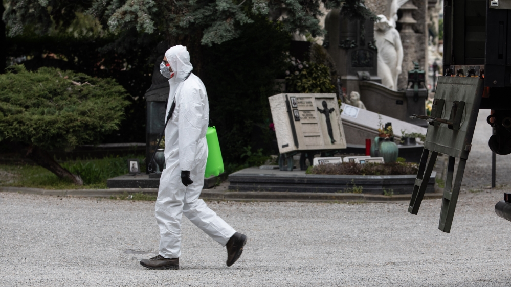 An Italian Army officer, wearing a protective suit, walks past a military vehicle in the Monumental Cemetery in Bergamo, near Milan
