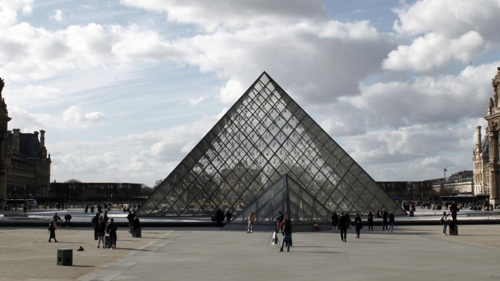 People walk by the Louvre Museum, in Paris, Friday, March 13, 2020. The Louvre Museum in Paris and the Versailles Palace both said that they are closing