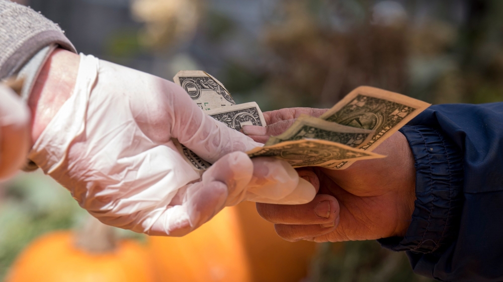 A shopper wearing protective gloves pays for a purchase with cash at a farmers market in San Francisco, California, U.S., on Wednesday, March 25, 2020. Fearful of close-quarters in packed supermarkets