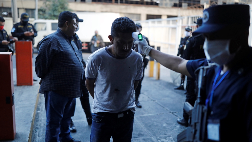 A police officer takes the temperature of a man detained for breaking a curfew imposed as part of measures against COVID-19 in Guatemala City