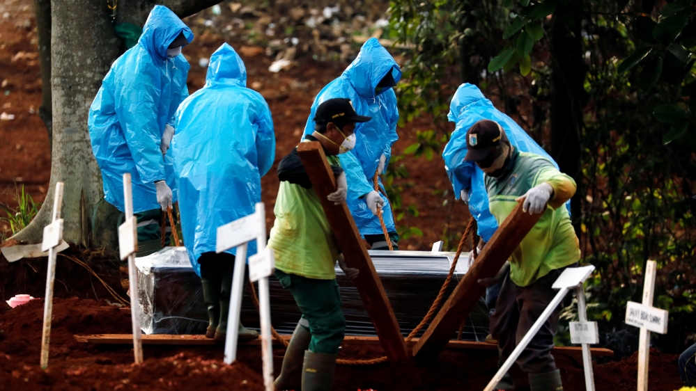 Municipality workers wearing raincoats as protective gear bury a COVID-19 victim at a cemetery in Jakarta, Indonesia