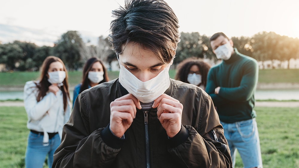 Young adult man wearing a pollution mask to protect himself from viruses. His friends are in the background. They all are wearing masks. Conceptual image of protection against pandemic virus.