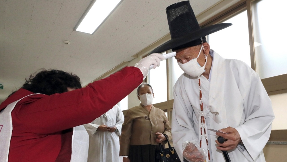 A South Korean Confucian scholar wearing a face mask to help protect against the spread of the new coronavirus has his temperature checked on arrival at a polling station