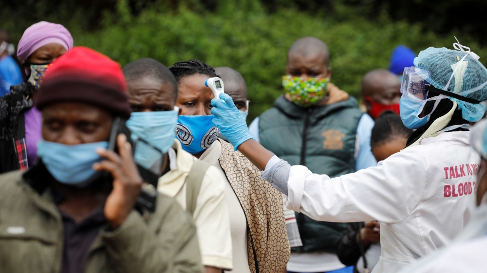A health worker takes the temperature of a person standing in line for mass testing in an effort to stop the spread of the coronavirus in the Kibera slum of Nairobi, Kenya