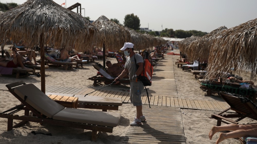 A man wearing a face mask disinfects a sunbed during the official reopening of beaches to the public following the easing of measures against the spread of the coronavirus disease (COVID-19), in Athens, Greece