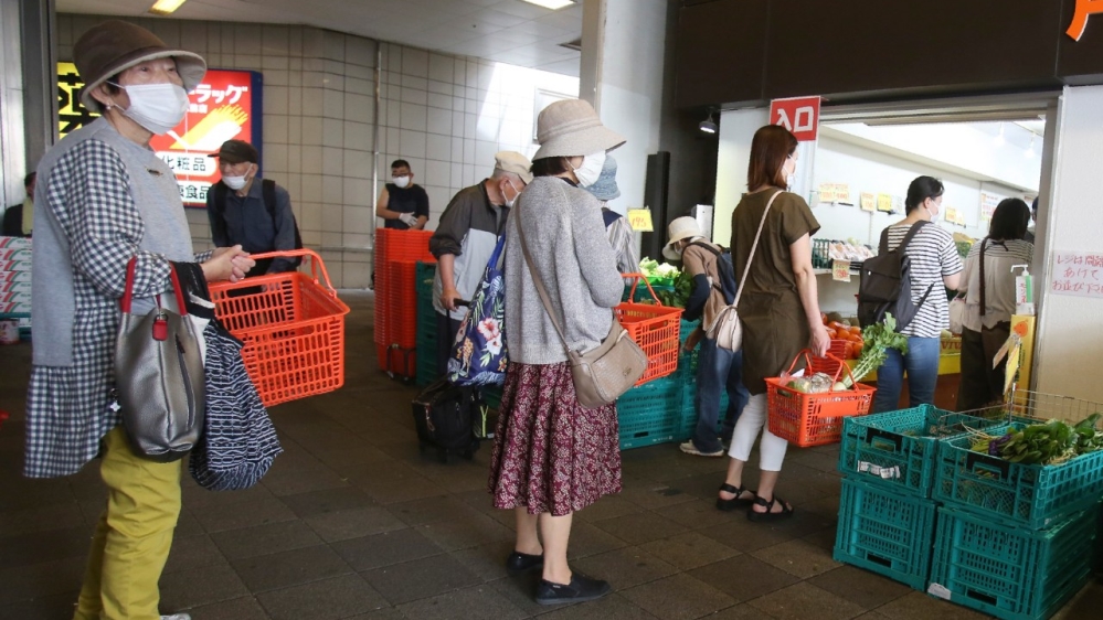 People observe physical distancing rules as they wait to enter a fruit and vegetable shop in Yokohama, Japan