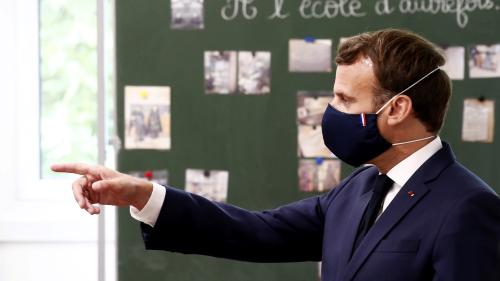 France’s President Emmanuel Macron wears a protective face mask with a blue-white-red coloured ribbon as he gestures while speaking with schoolchildren at an elementary school in Poissy