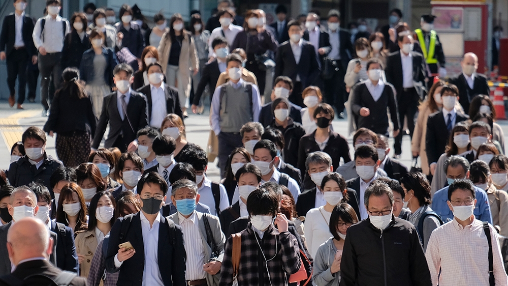 Commuters wearing face masks cross a street by a railway station in Tokyo on May 7