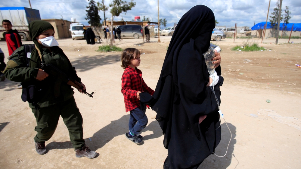 A fighter of Syrian Democratic Forces (SDF) walks with the wife of an Islamic State fighter, who holds her sick baby, at al-Hol displacement camp in Hasaka governorate