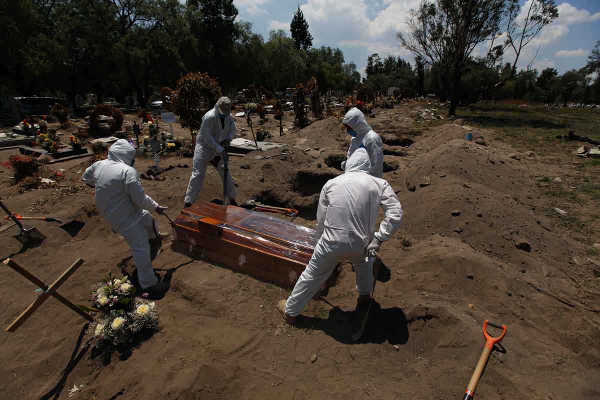 Cemetery workers in a protective gear lower a coffin wrapped in plastic, containing a COVID-19 victim, into a gravesite at the San Lorenzo Tezonco Iztapalapa cemetery in Mexico City, Tuesday, June 2,