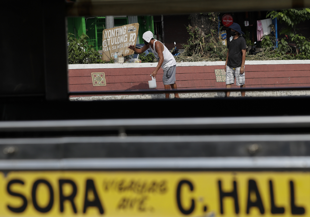 Jeepney drivers beg for money beside a sign that says "a little help please for the drivers, thank you" in front of the Tandang Sora terminal which have been home for them since a lockdown started thr