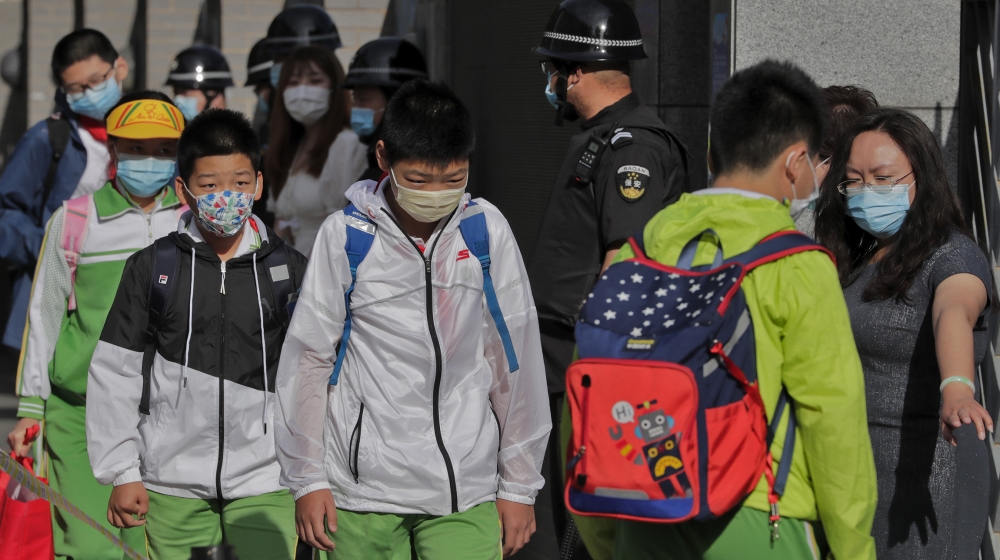 Students wearing protective face masks to help curb the spread of the new coronavirus are directed by a teacher to keep their social distancing as they arrive for the reopening of a primary school in 
