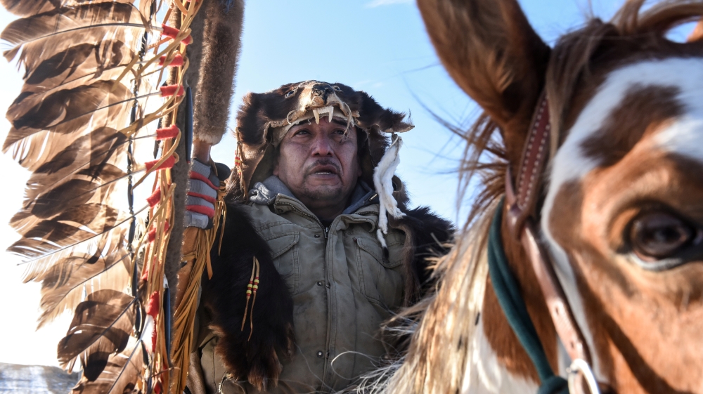 A Lakota person rides a horse with a sacred staff during a trip to meet Brad Upton, a descendant of the commander of the Wounded Knee massacre, part of a bloody history between the Lakota and the US