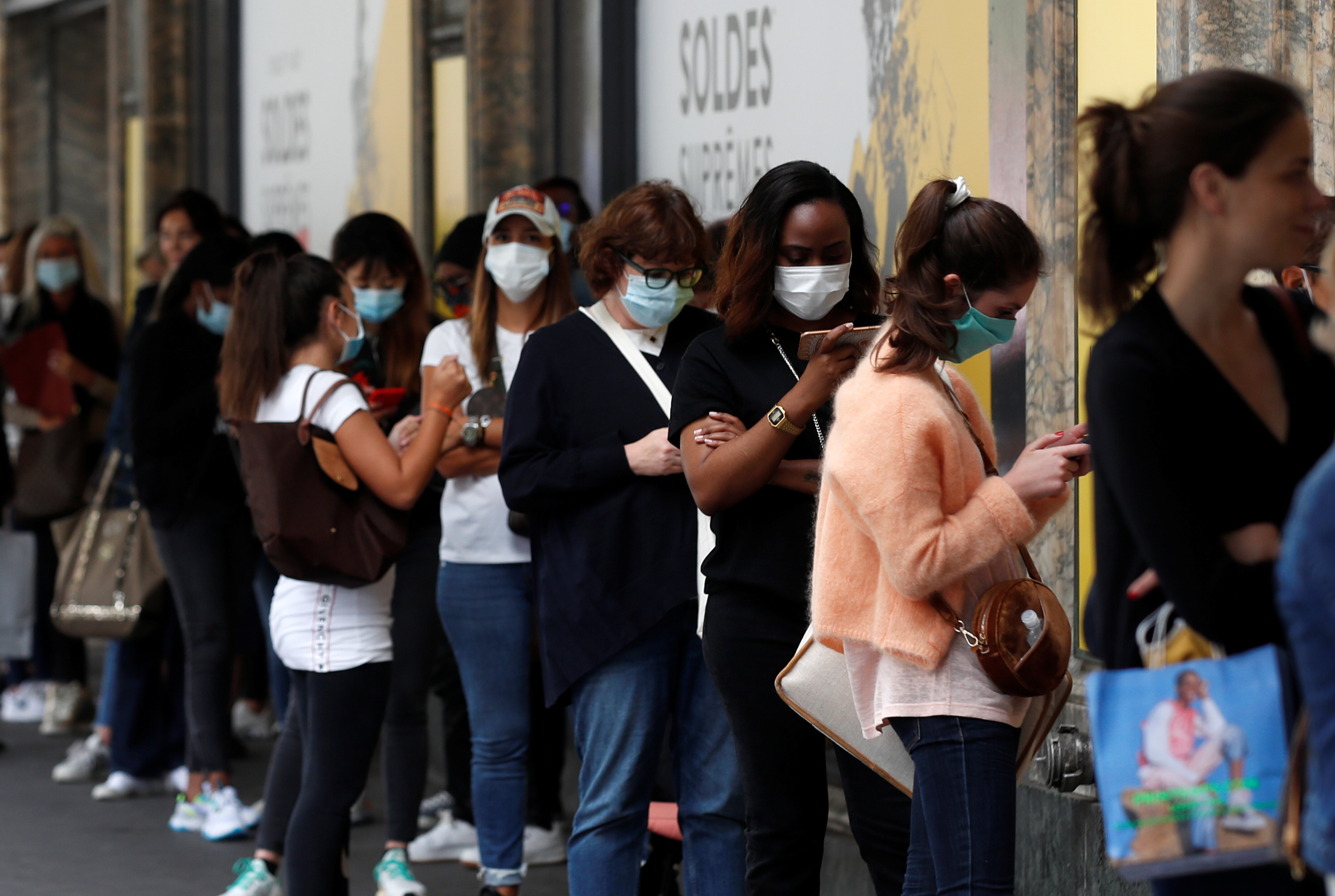 People wearing protective face masks queue at a department store in Paris