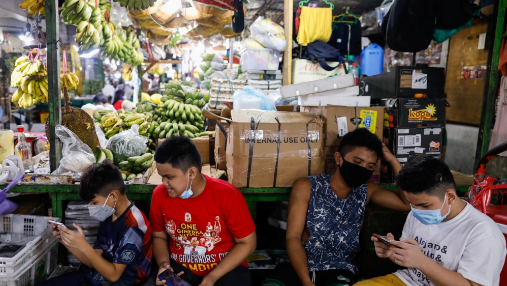 Children wearing face masks for protection against the coronavirus disease play video games on their phones at a market in Quezon City, Metro Manila
