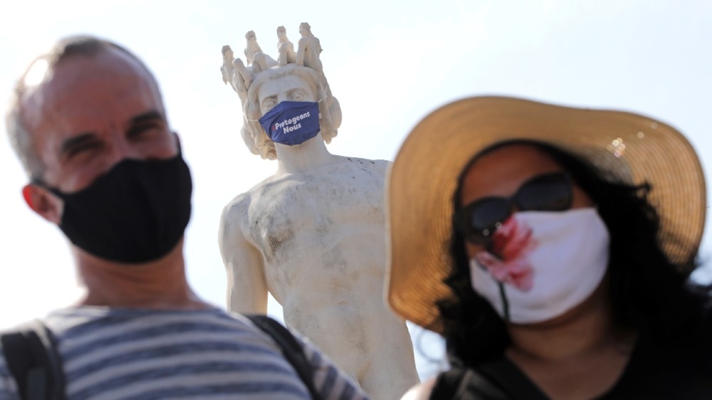 Tourists in protective masks stand by a masked statue that reads, ‘Let’s protect ourselves’ in Nice as France reinforces mask-wearing as part of efforts to curb a resurgence of COVID-19 across the country