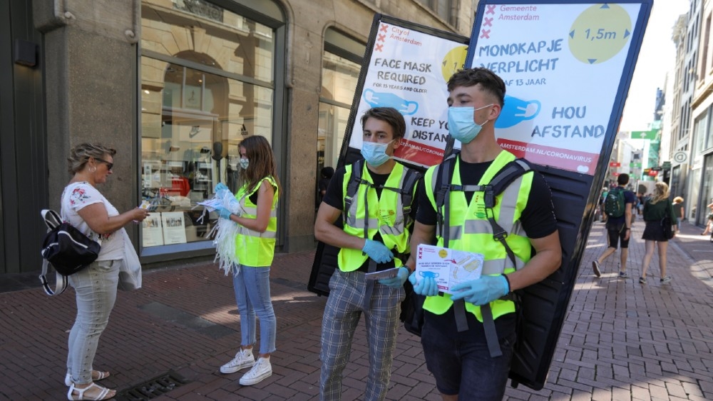 People wearing yellow vests hand out masks and information brochures where to wear the mandatory masks in the busiest streets of the city, during the coronavirus disease (COVID-19) outbreak, in Amsterdam, Netherlands