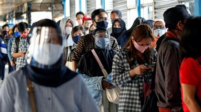 Passengers wearing protective masks and face shields queue for a public bus in Jakarta