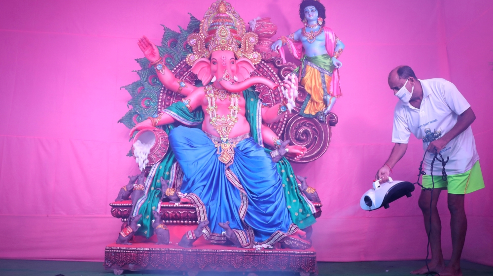 A Hindu devotee wearing a protective mask sanitises a pandal, or a temporary platform, next to an idol of Hindu god Ganesh in Kolkata city