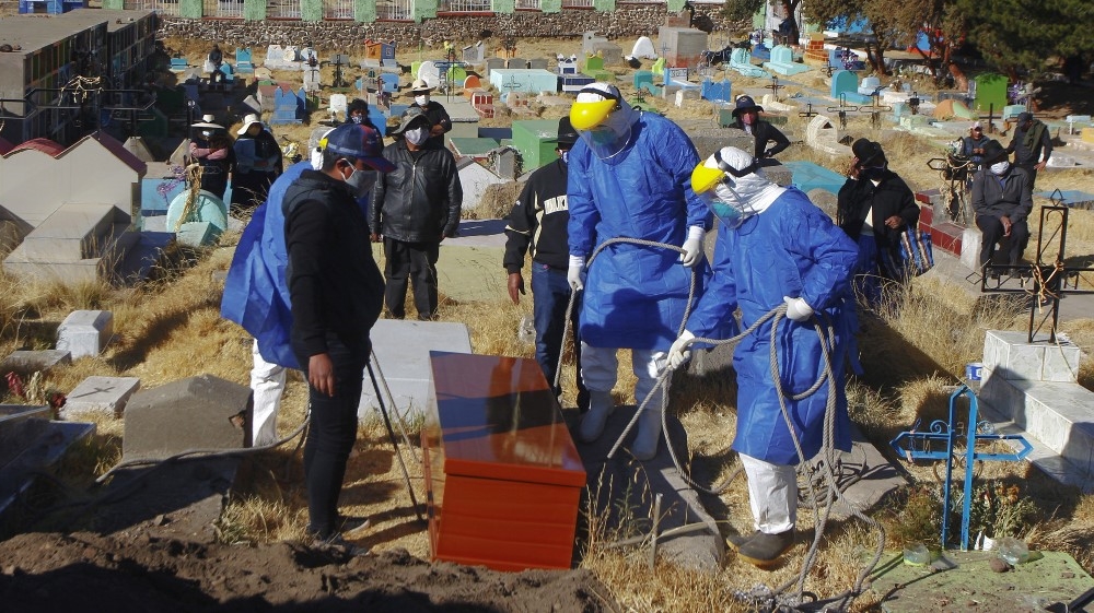 Funerary employees in protective suits prepare to lower the coffin into the ground during the burial of a COVID-19 patient at the local cemetery in the remote Aymara highland village of Acora, close to the border with Bolivia, on August 9, 2020