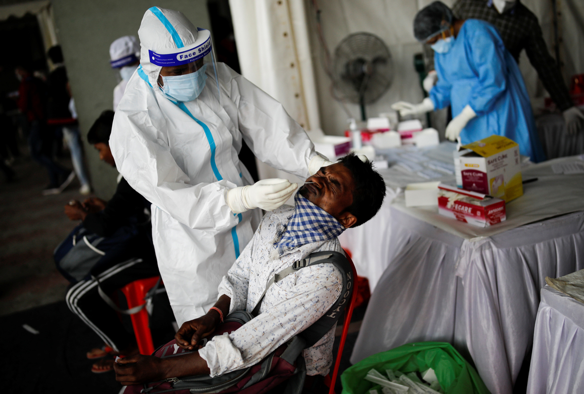 A healthcare worker wearing personal protective equipment (PPE) takes a swab from a migrant worker, who returned to Delhi from his native state, for a rapid antigen test at a bus terminal, amidst the