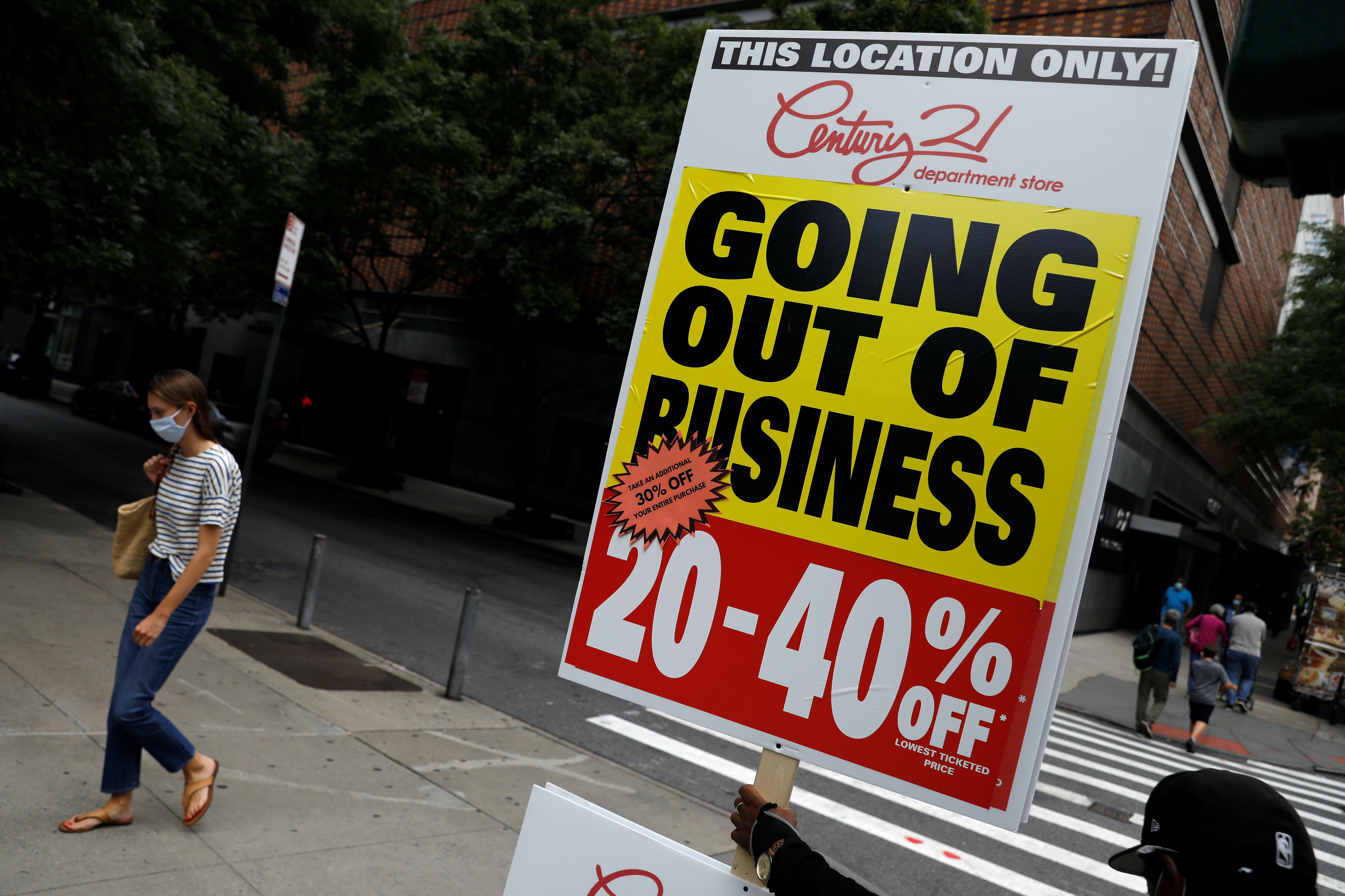 A person holds a sign advertising a sale at Century 21, a retail outlet that announced it was filing for bankruptcy and closing its stores due to the economic impact of the coronavirus in Manhattan, New York, US