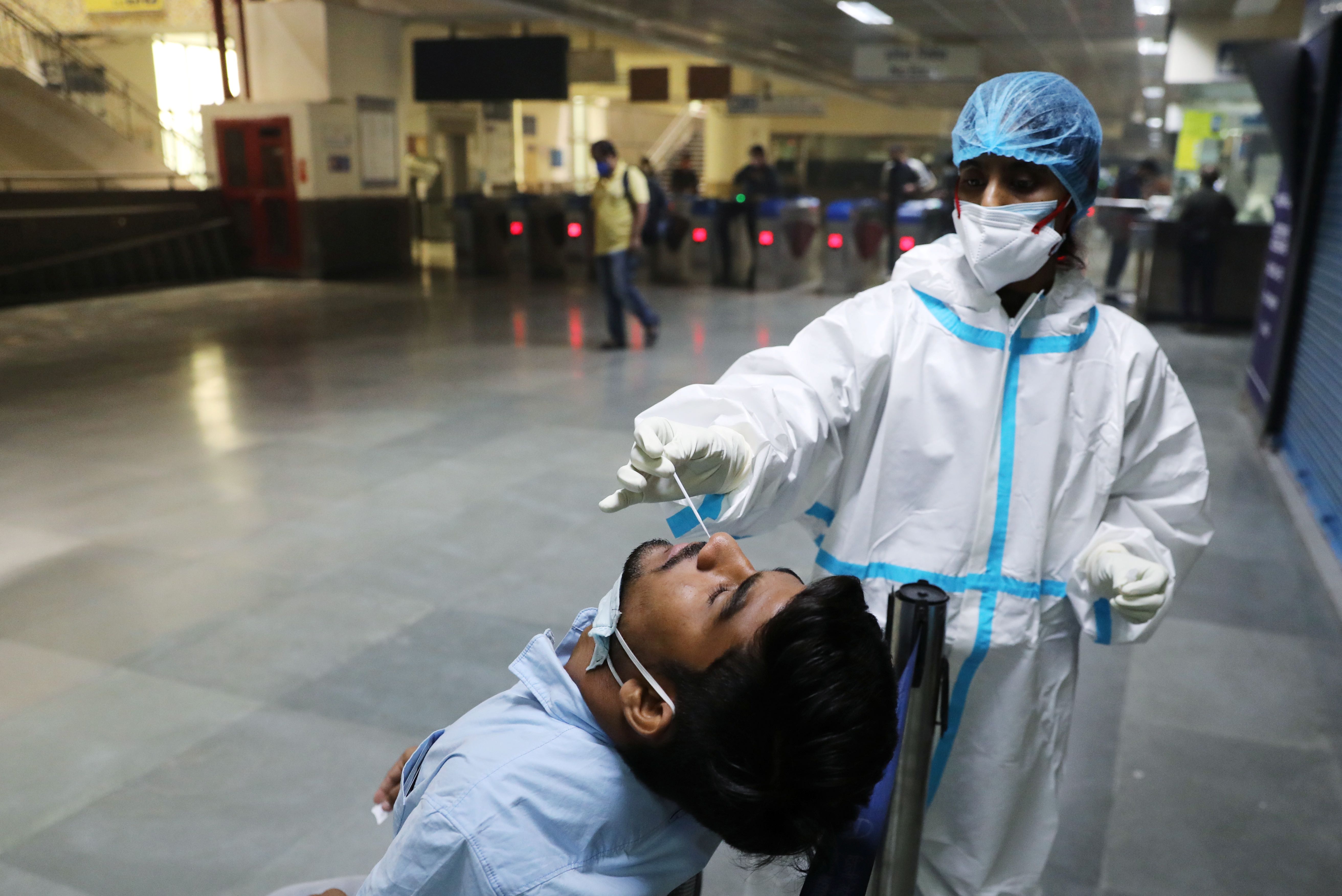 A healthcare worker wearing personal protective equipment collects a swab sample from a man amid the spread of the coronavirus at a metro station, in New Delhi, India