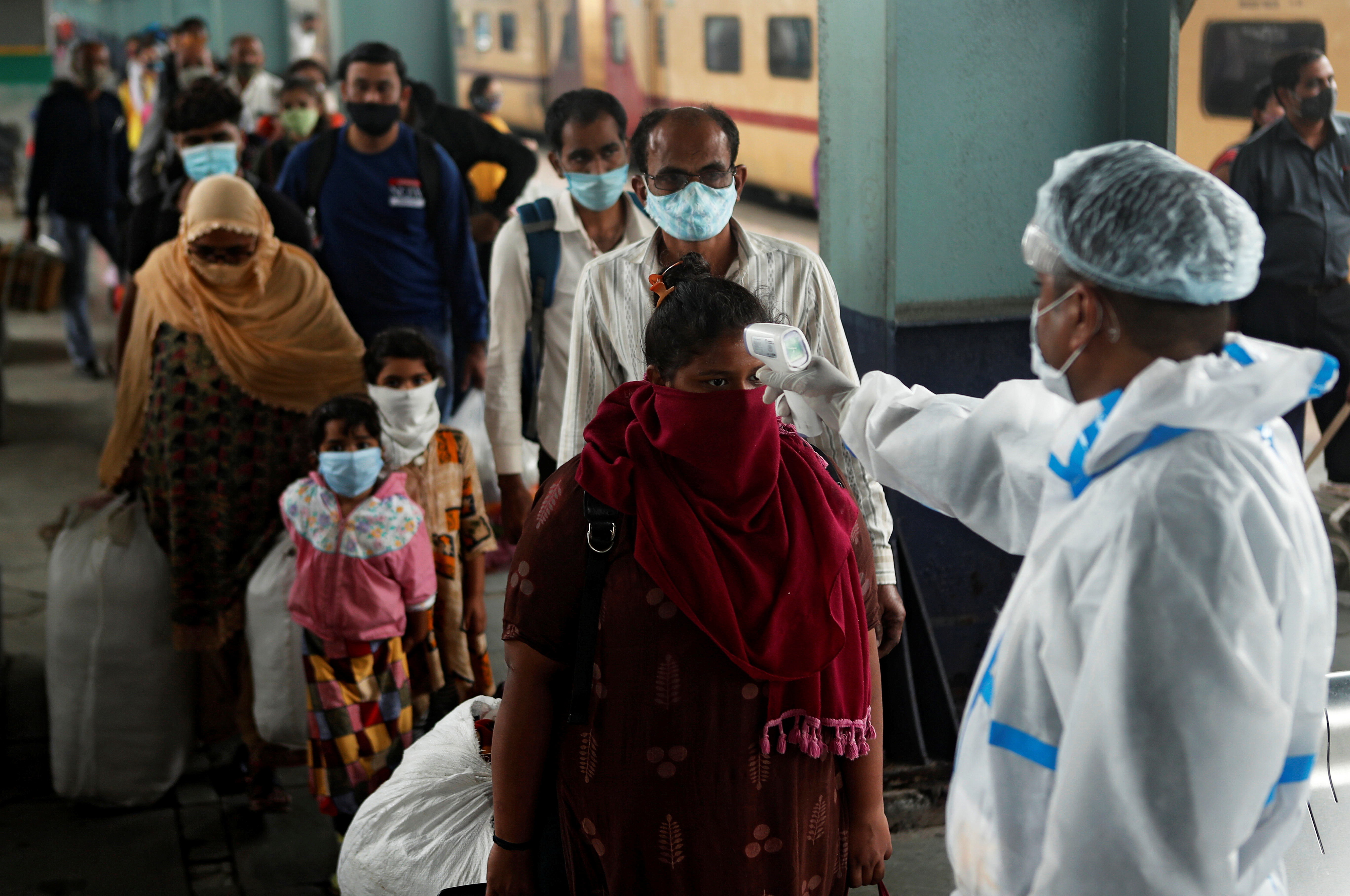 A health worker in personal protective equipment checks the temperature of passengers at a railway station in Mumbai, India