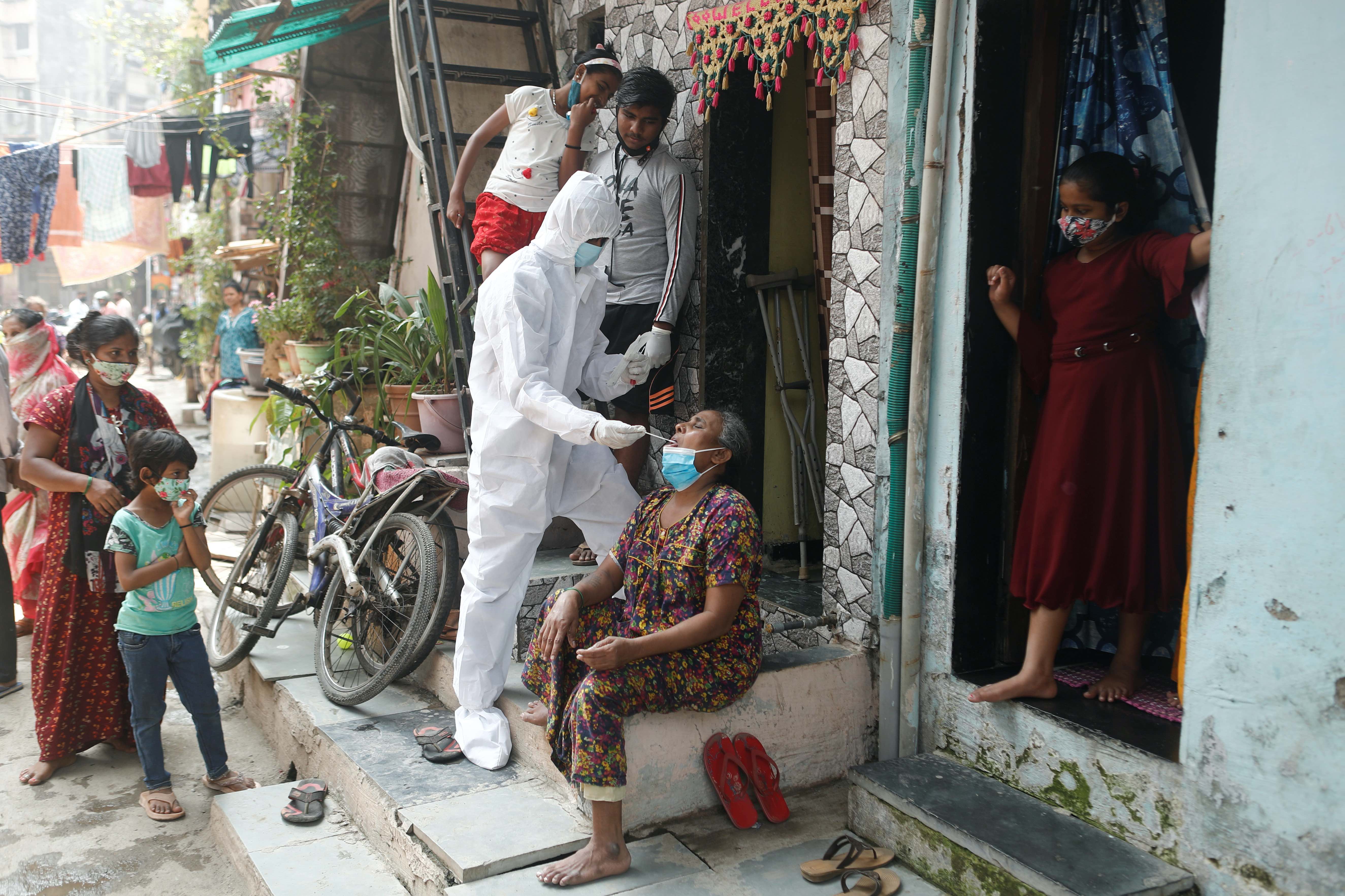 A healthcare worker in personal protective equipment collects a swab sample from a resident during a testing campaign for the coronavirus in Mumbai, India