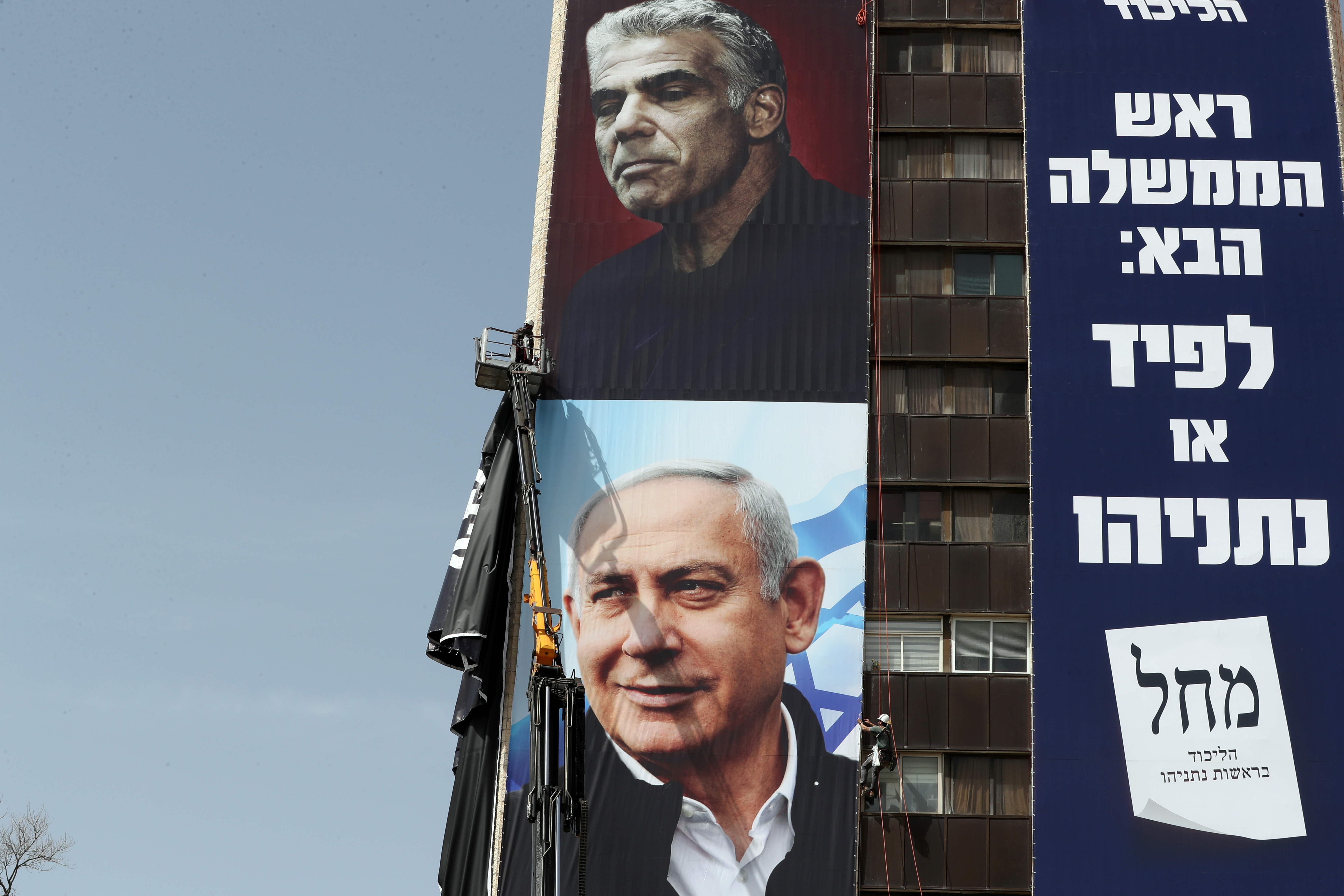 Labourers hang a Likud party election campaign banner depicting party leader Israeli Prime Minister Benjamin Netanyahu and his challenger Yesh Atid party leader Yair Lapid, ahead of a March 23 ballot, in Jerusalem March 10, 2021. The writing in Hebrew reads: 'Next Prime Minister: Lapid or Netanyahu". [Ammar Awad/Reuters]