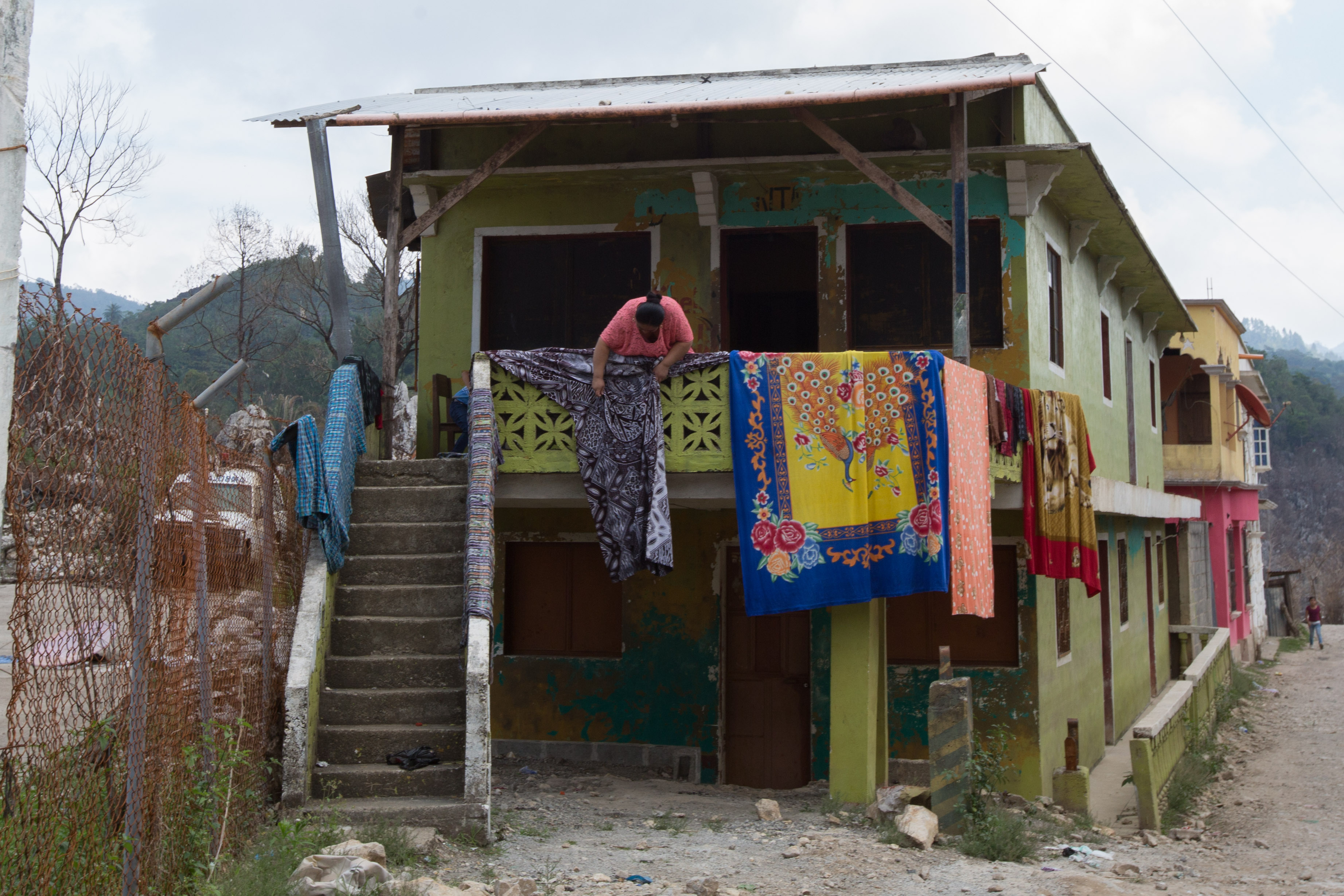 A woman hangs blankets along the side of her house, which was damaged by the November 2020 flooding in Campur