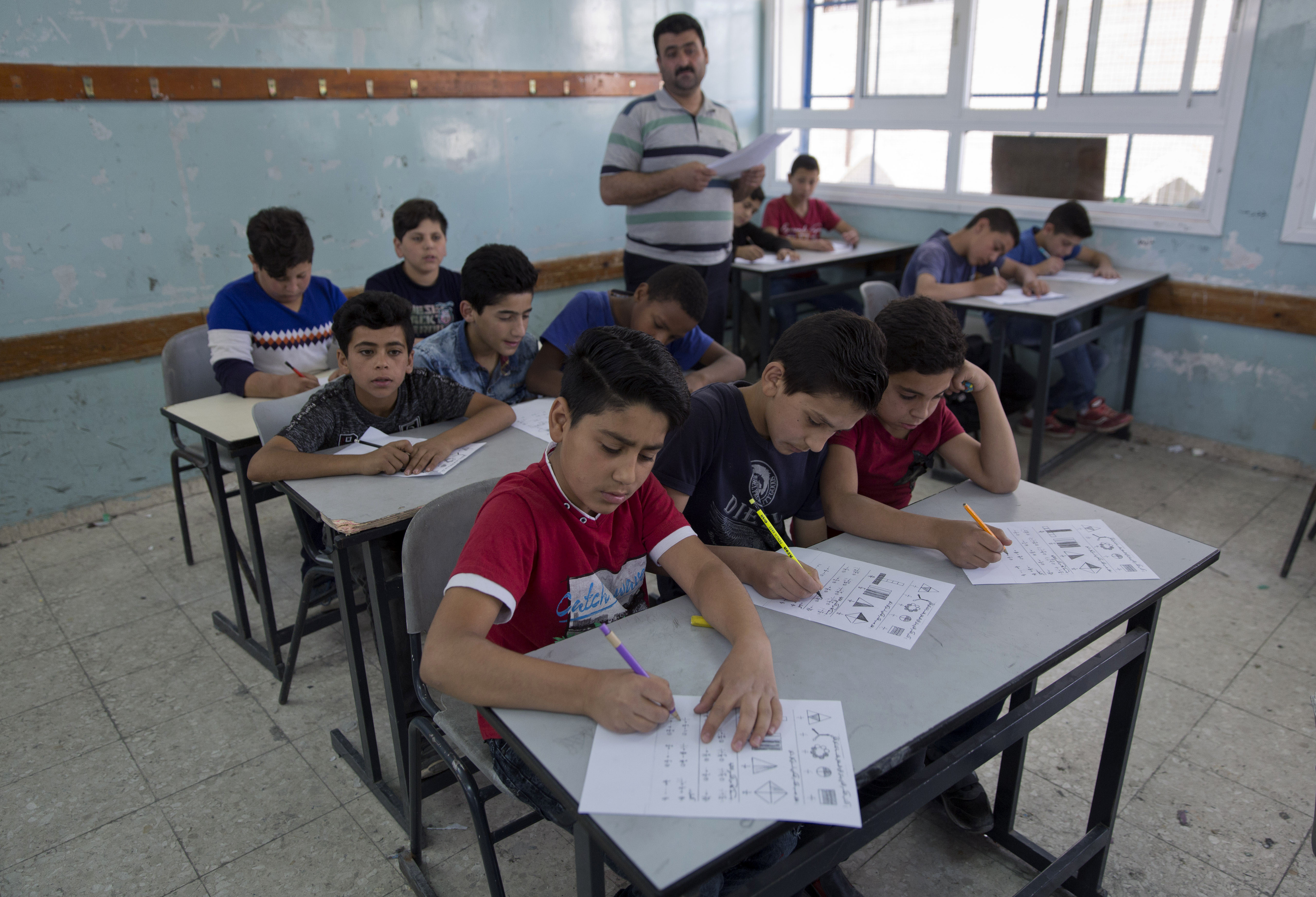 kids sitting and writing their exams in a light blue classroom of an unrwa school