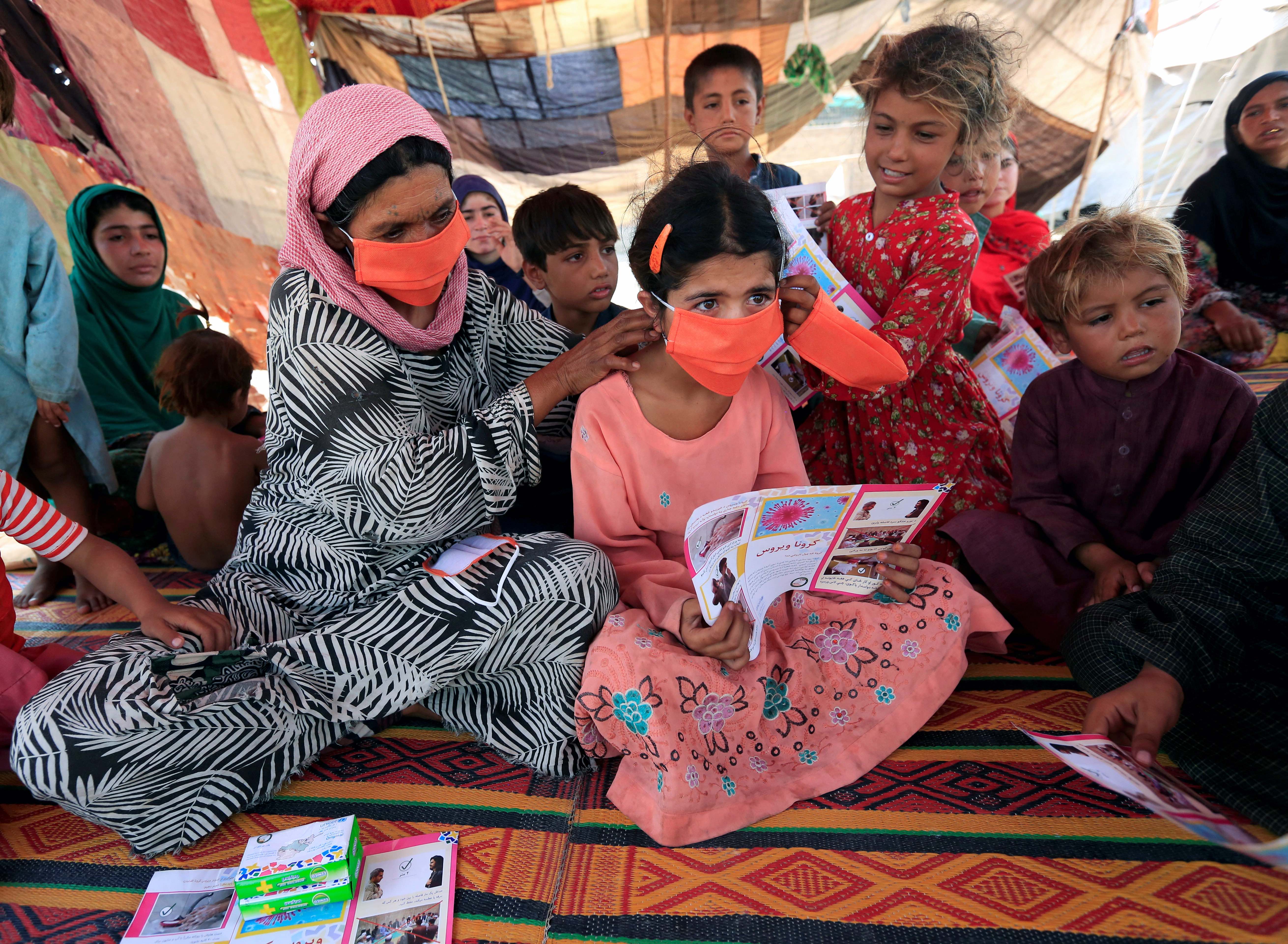 An internally displaced woman helps a girl put on a face mask distributed by UNICEF at a makeshift camp amid the coronavirus outbreak in Jalalabad, Afghanistan