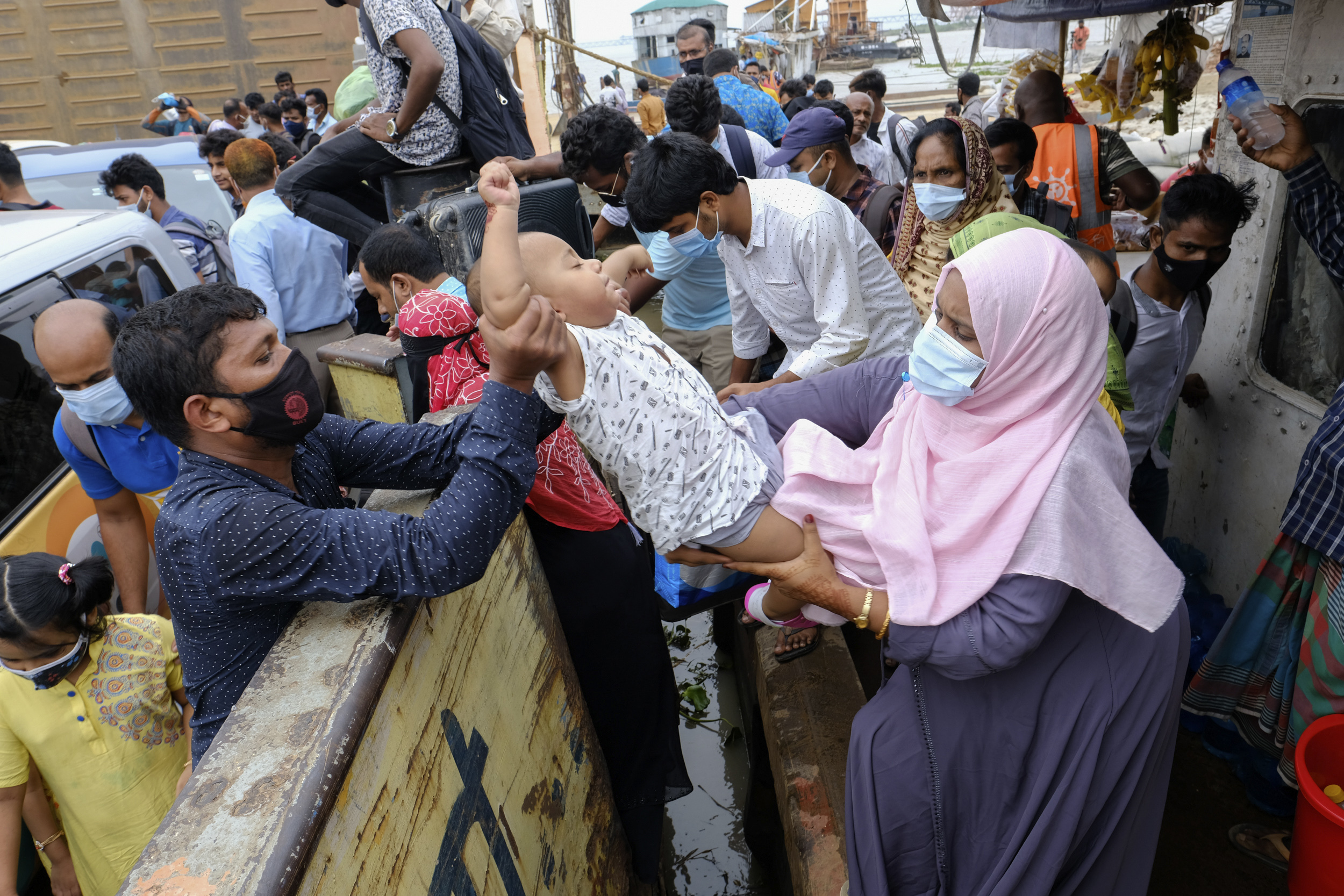 A child is handed over to board a ferry as people crowd a ferry terminal to leave Dhaka ahead of a lockdown set to start on Thursday