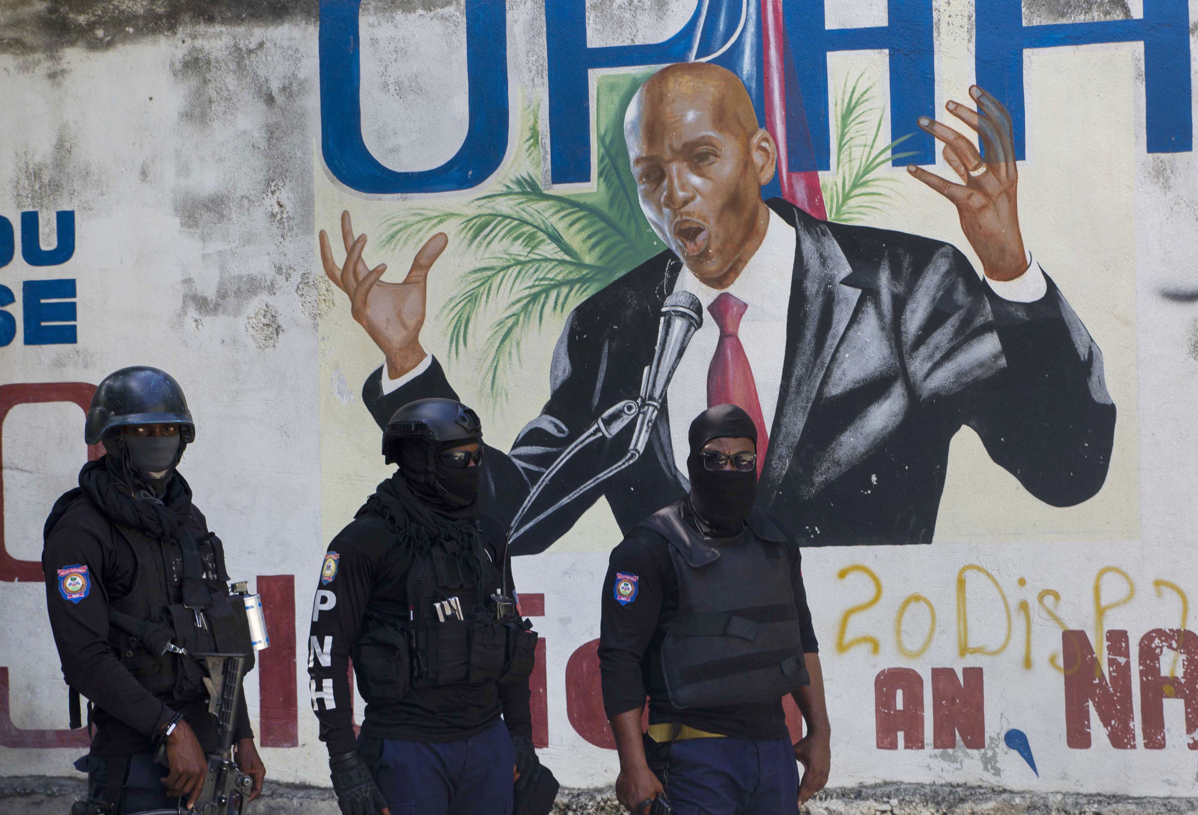 Police stand near a mural featuring Haitian President Jovenel Moise near the leader’s residence where he was killed by gunmen in the early morning hours of July 7