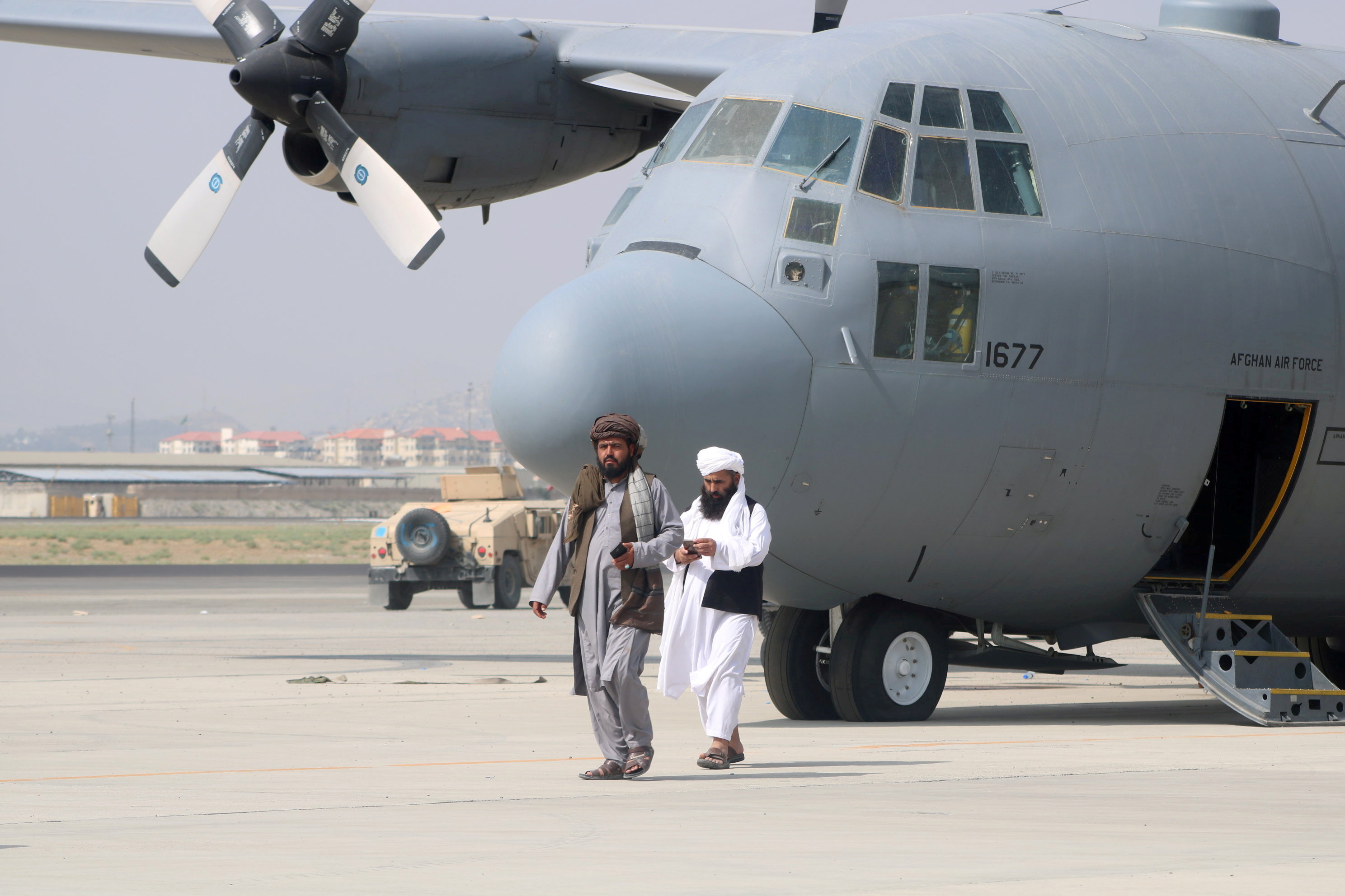 Taliban walk in front of a military aeroplane