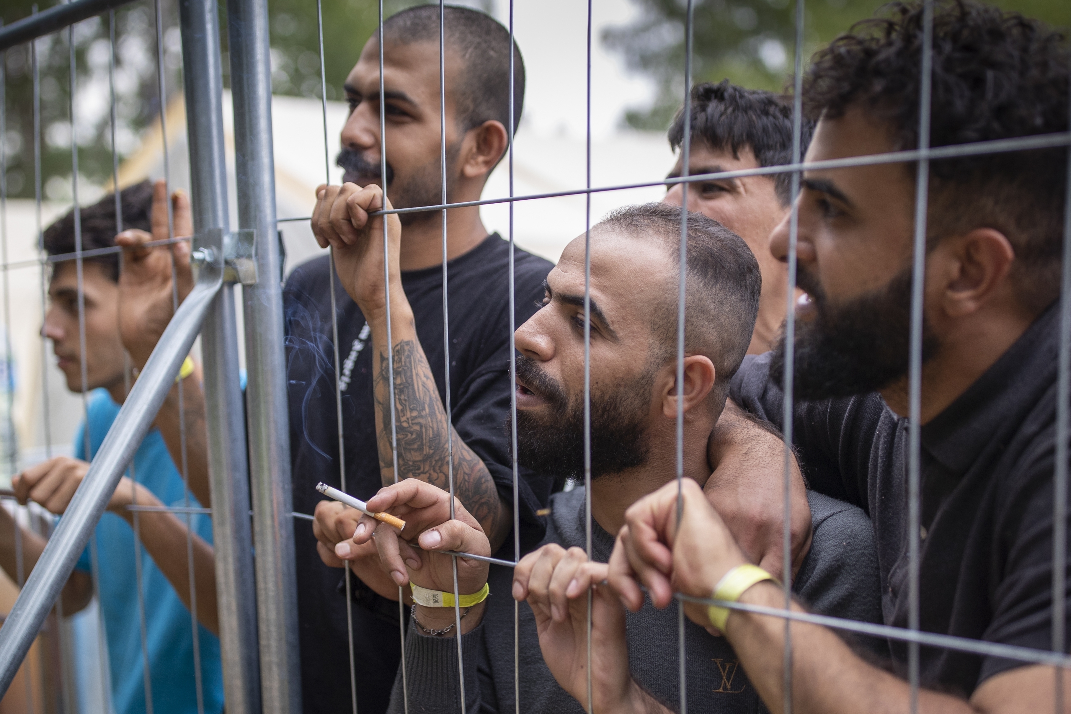 Refugees and migrants stand at the fence at the newly built refugee camp in the Rudninkai military training ground, 38km (23.6 miles) south of Vilnius, Lithuania, in 2021. [File: Mindaugas Kulbis/AP]