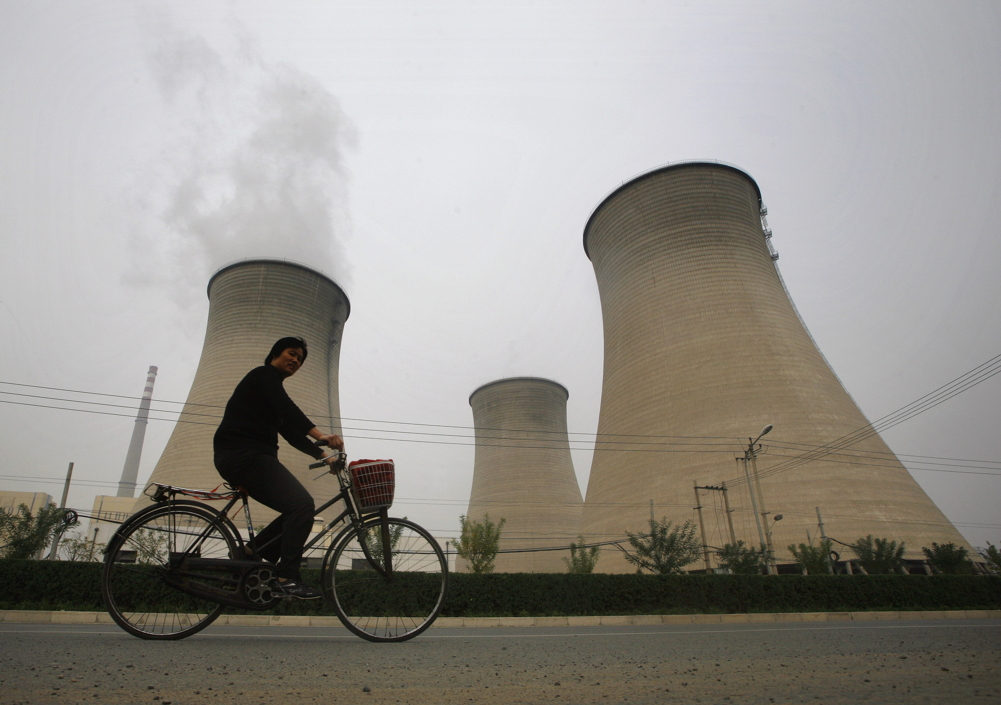 man cycles past China power station