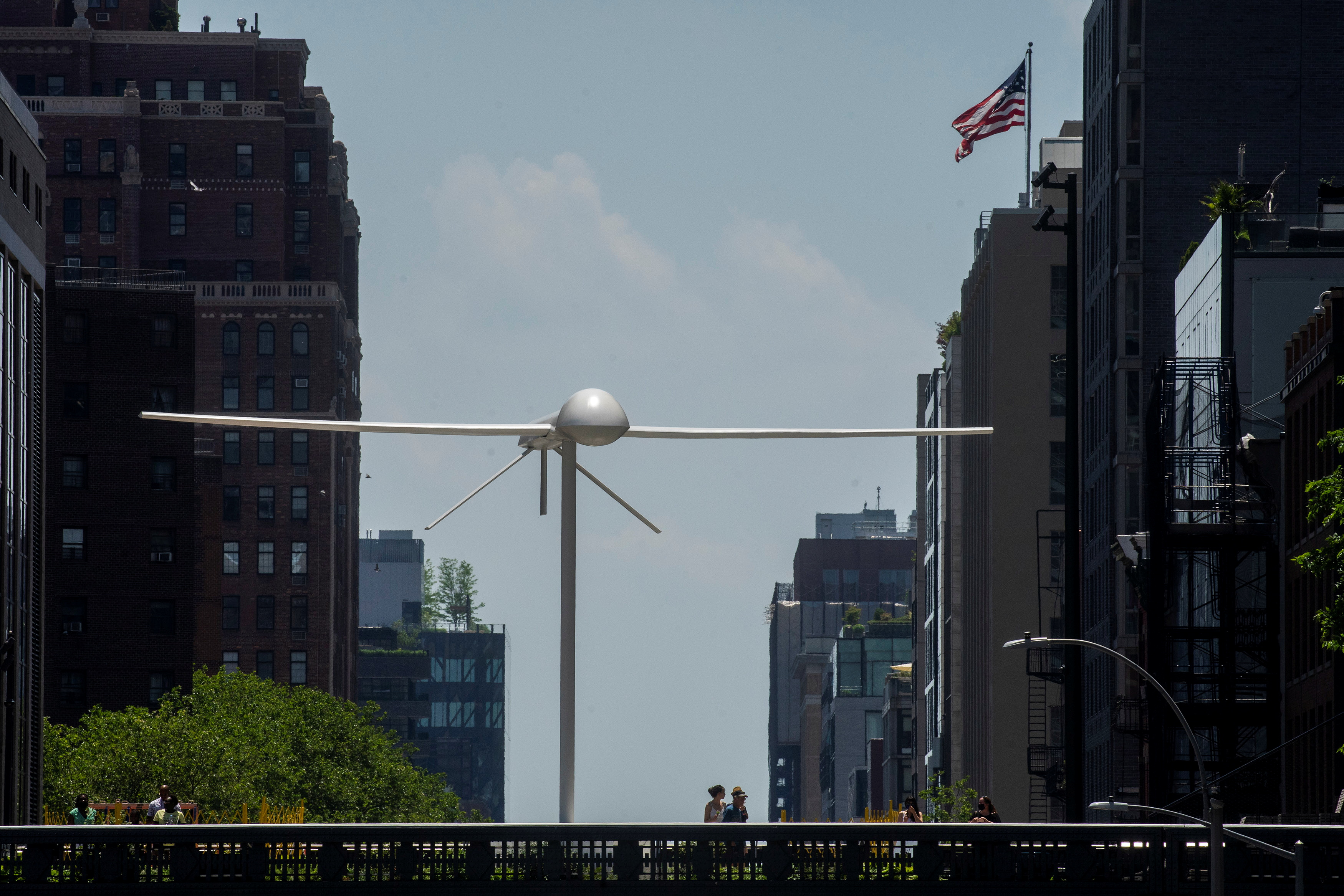 People walk near a sculpture by artist Sam Durant called 'Untitled' (drone), a fibreglass sculpture depicting a Predator drone, as it is seen over the High Line park in Manhattan borough of New York, on June 6, 2021 [File: Eduardo Munoz/Reuters]