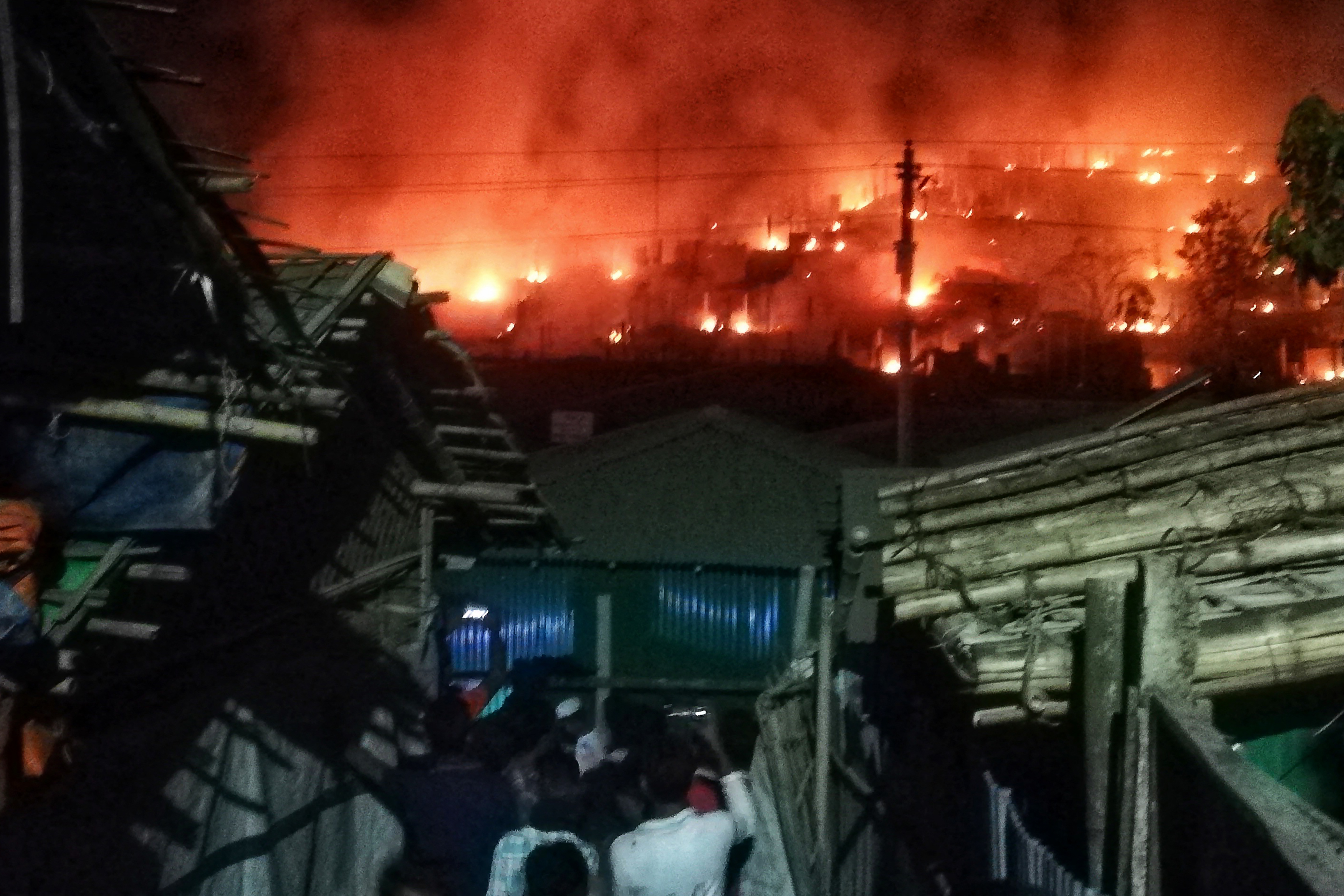 Onlookers gather as smoke and flames can be seen on a hillside after a fire broke out in a Rohingya camp