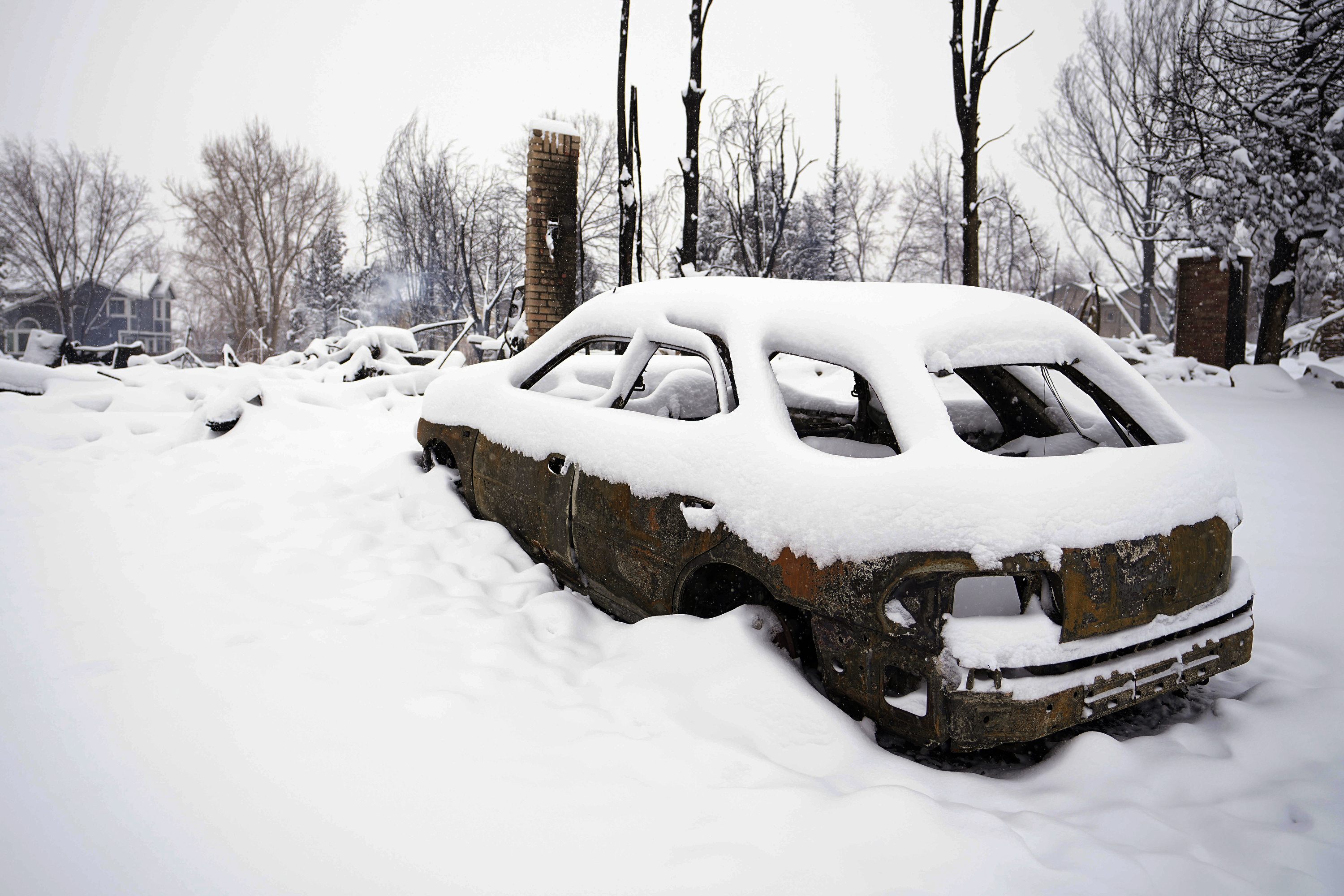 Snow covers the burned remains of a vehicle in the Marshall Wildfire in Colorado