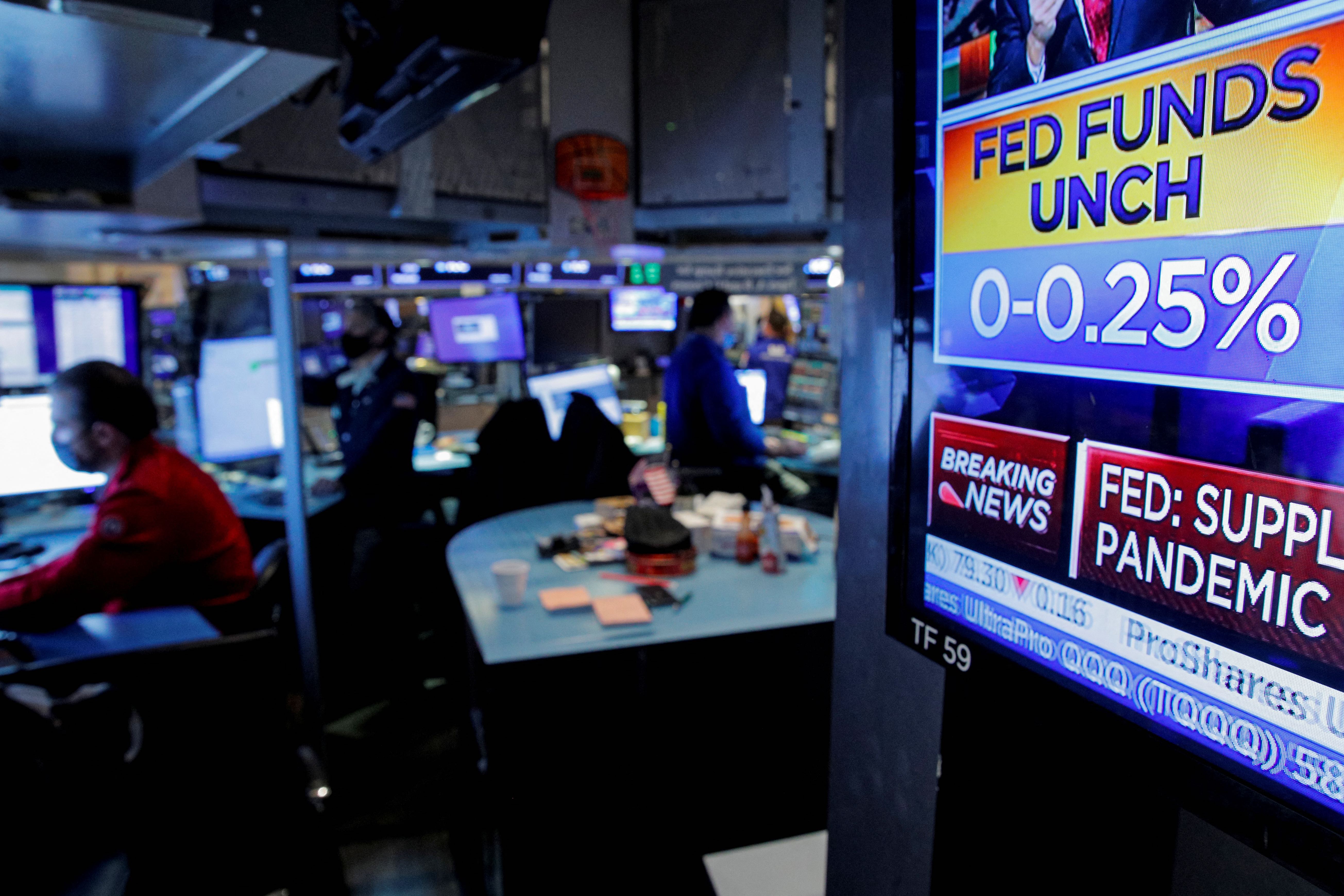 A screen displays the Fed rate announcement as traders work on the floor of the New York Stock Exchange