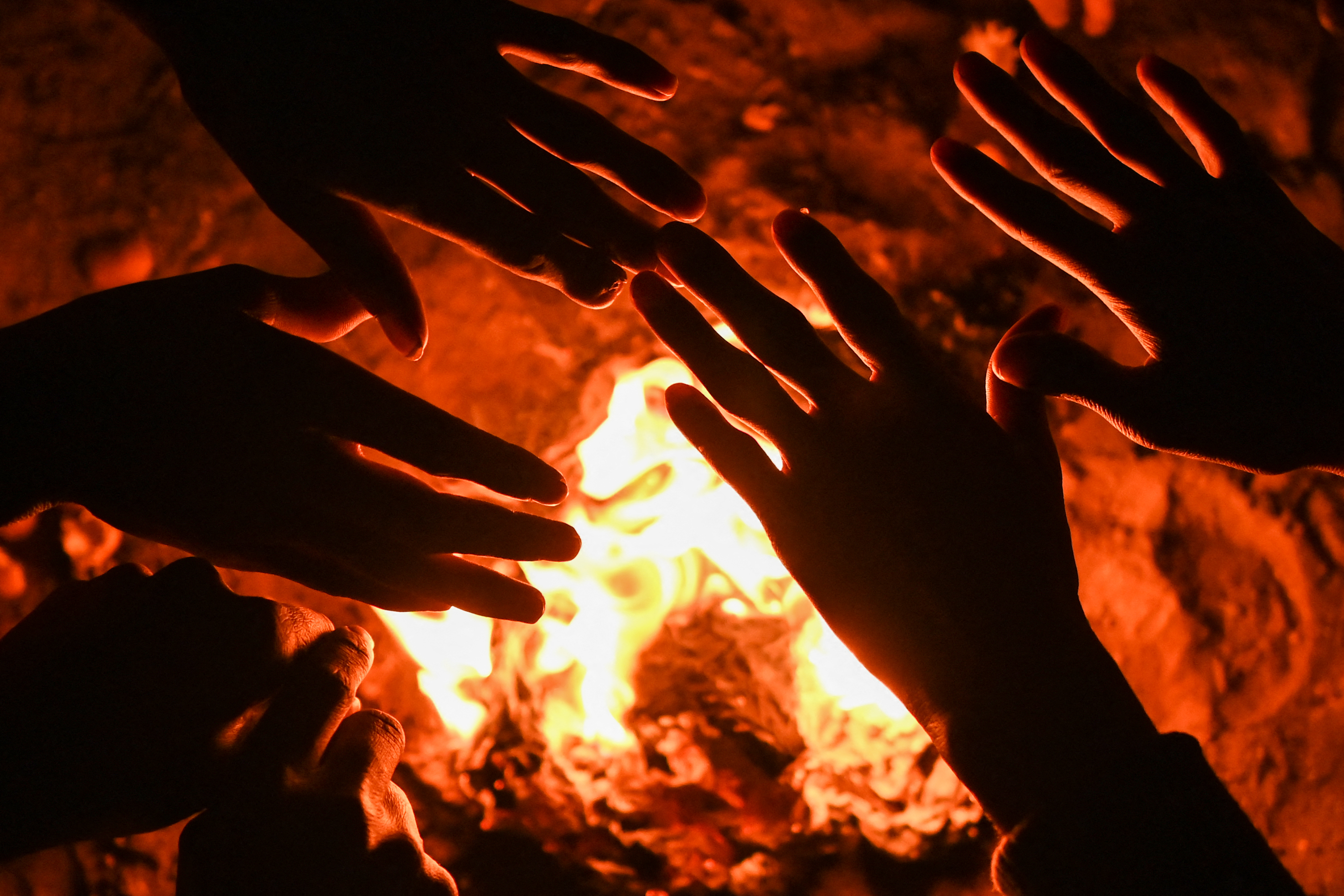 In this picture taken on January 29, 2022, shows homeless people gathered besides a bonfire to keep themselves warm in a wintry evening in New Delhi.