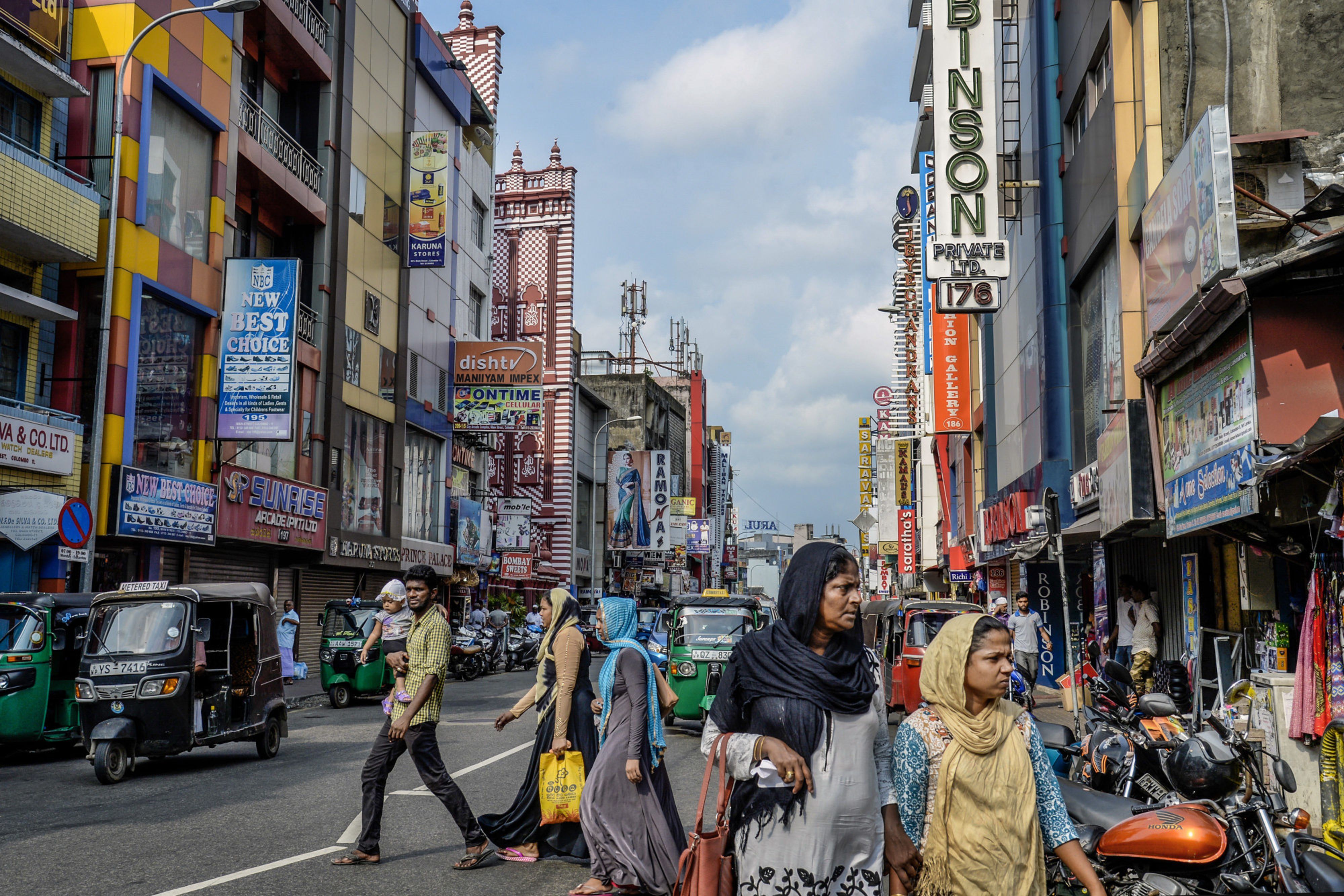 Shoppers and pedestrians walk past auto-rickshaw on a shopping street in Colombo, Sri Lanka